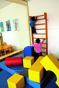 zwei Kinder erklettern eine Sprossenwand, davor liegen viele Bewegungsbausteine