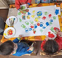 Kinder drucken mit bunter Fingerfarbe ihre Hände auf ein gemeinsames Plakat
